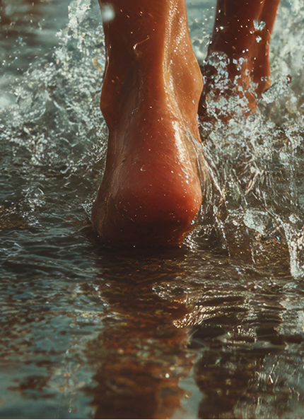 Rear close-up of a foot walking on the beach, in the water