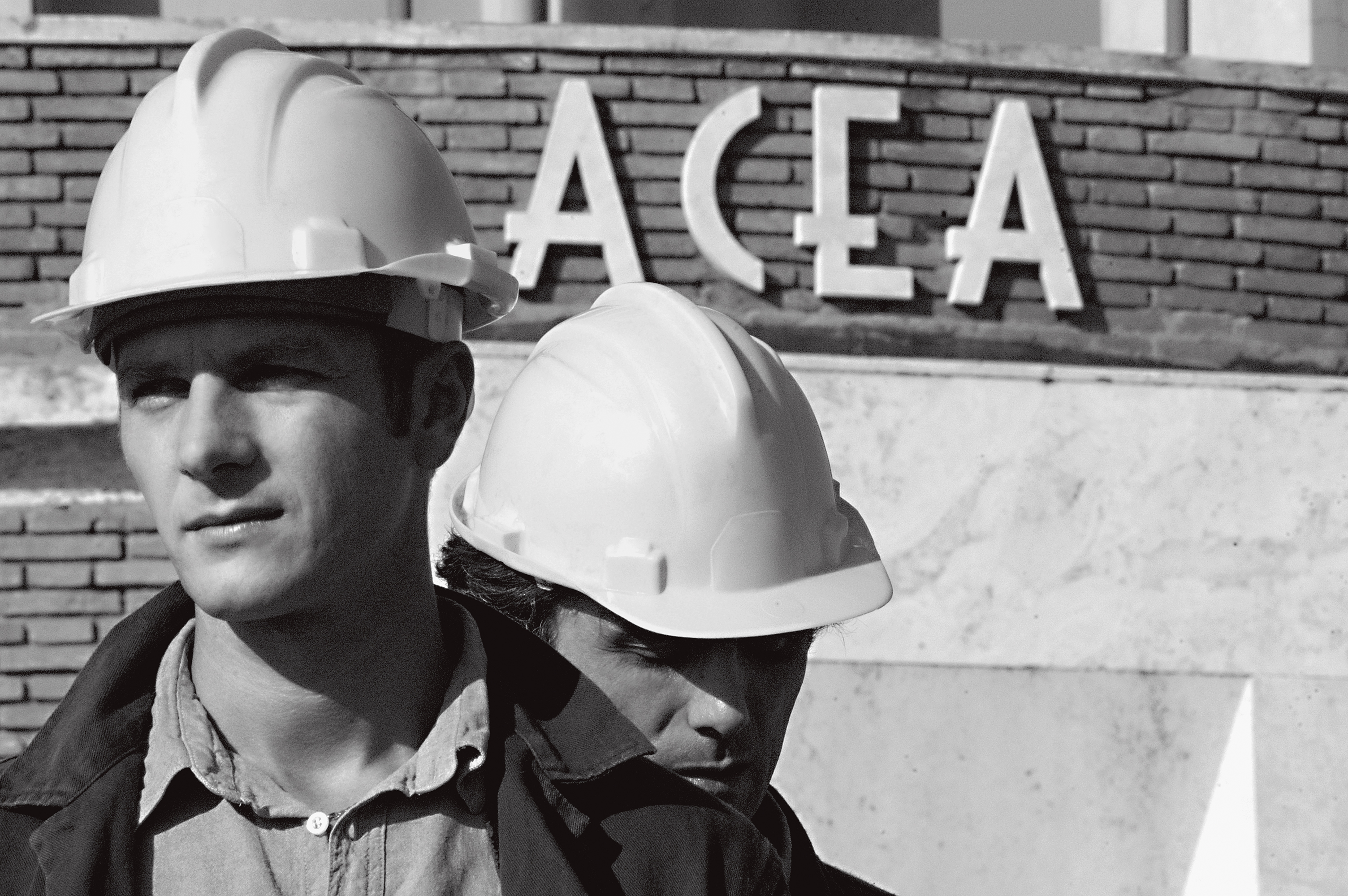 Black and white photo of two workers wearing helmets with the Acea logo in the background