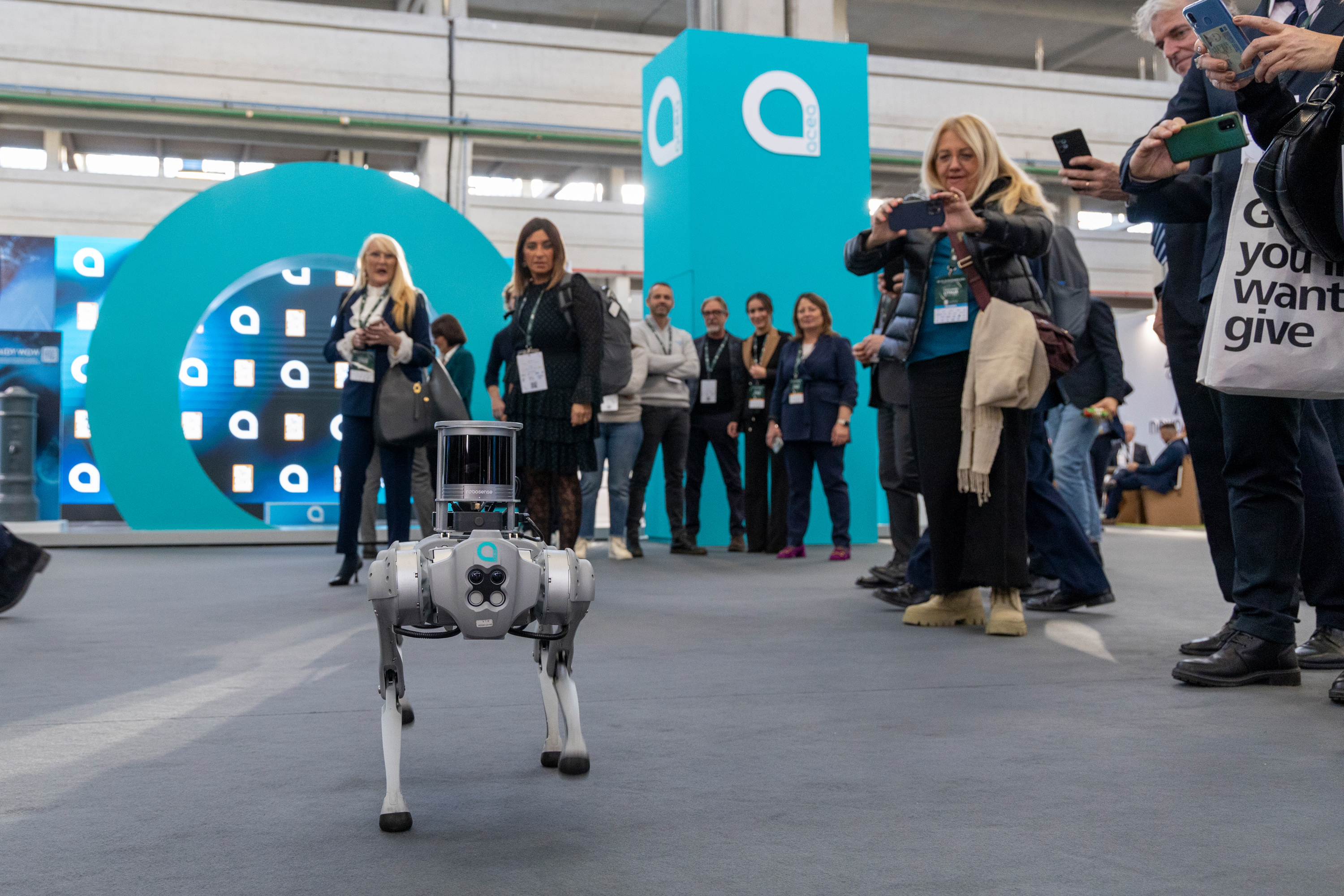 Group of attendees at the event looking at and photographing the dog-shaped robot