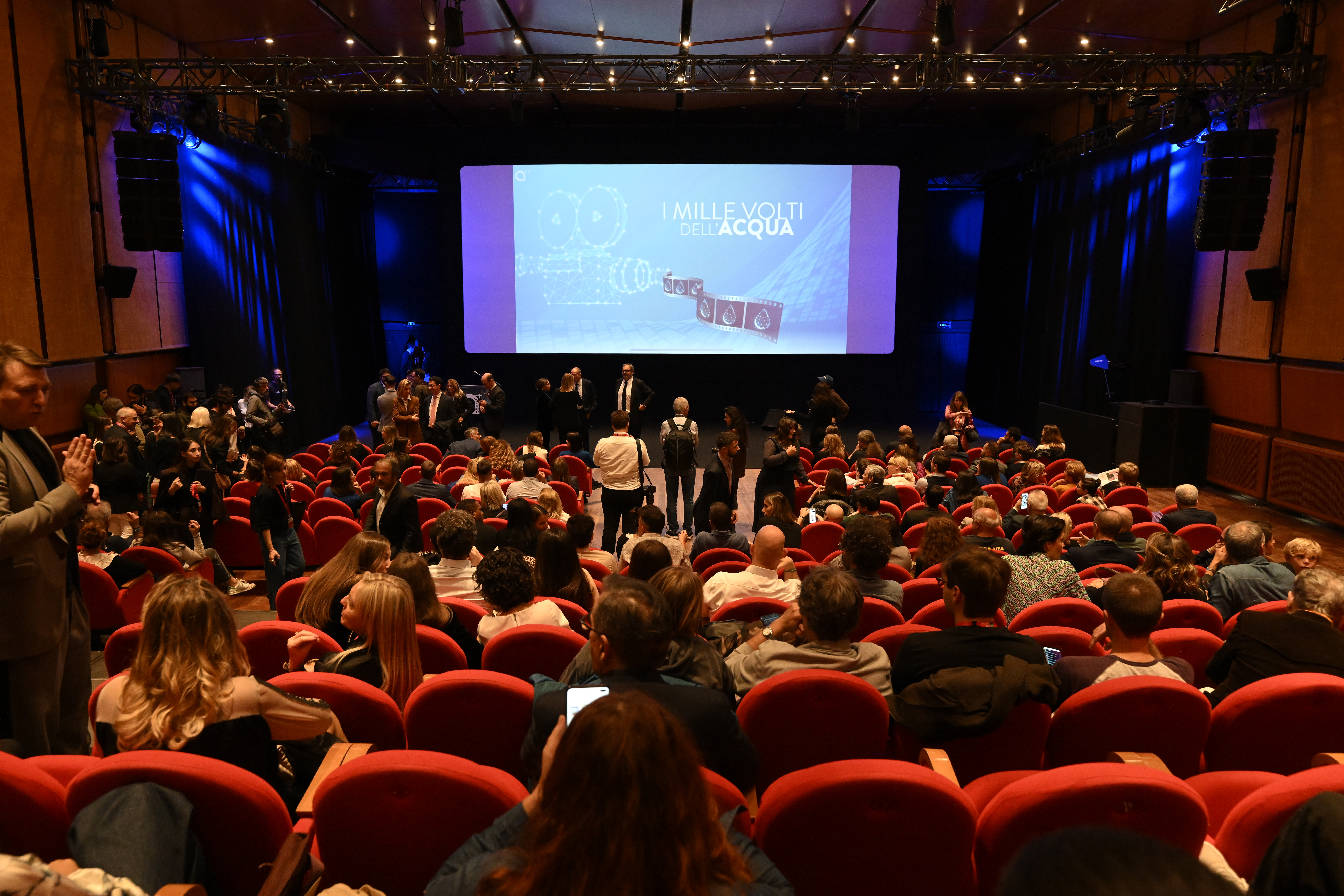 A room full of people and in the background a lit screen showing ‘The Thousand Faces of Water’.