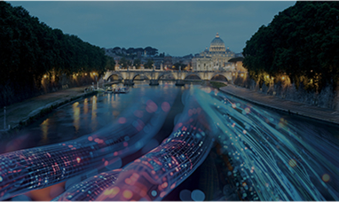 In the background in the Vatican and in front of it a bridge, both illuminated. Coloured electric cables run over the Tiber