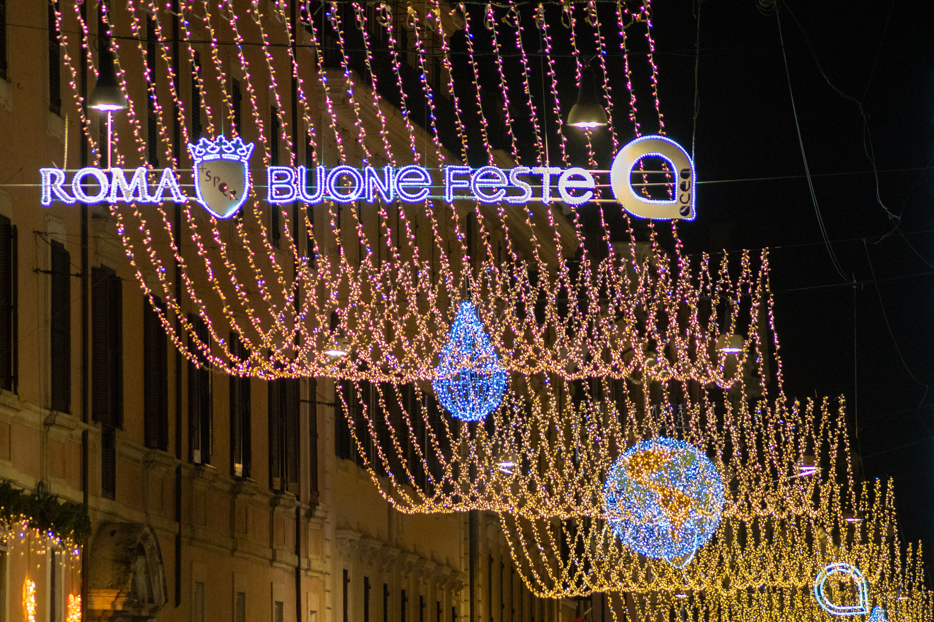 Primo piano delle luminarie accese con la scritta illuminata "roma buone feste" e il logo Acea