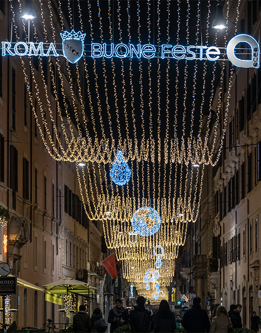 Primo piano delle luminarie accese con la scritta illuminata "roma buone feste" e il logo Acea