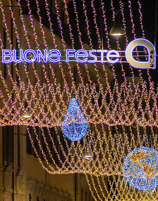 Primo piano delle luminarie accese con la scritta illuminata "roma buone feste" e il logo Acea