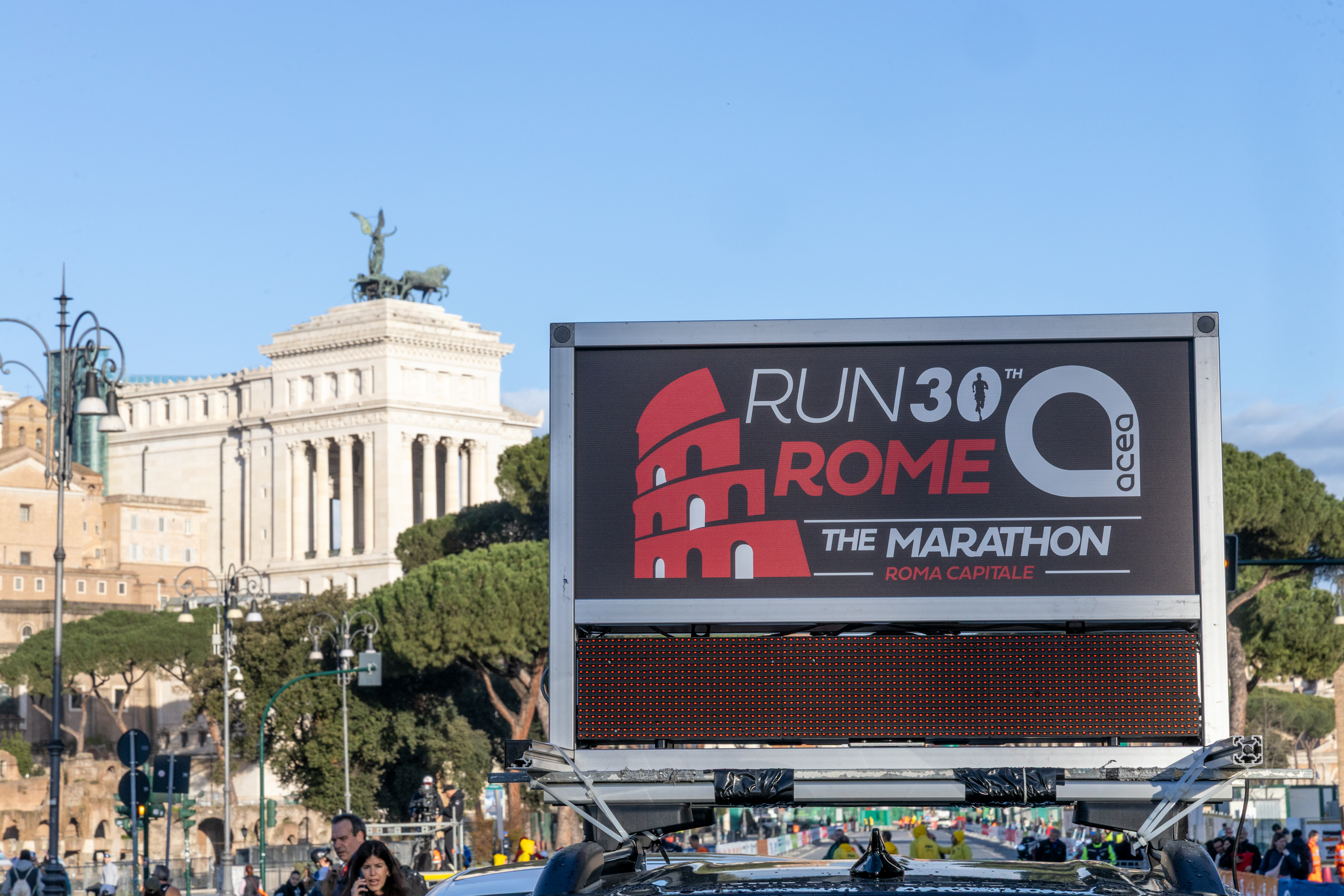 Event poster with the words ‘run rome 30 the marathon’ and the acea logo. Behind the billboard you can see the altare della Patria