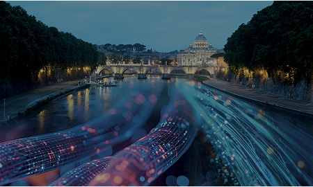In the background in the Vatican and in front of it a bridge, both illuminated. Coloured electric cables run over the Tiber