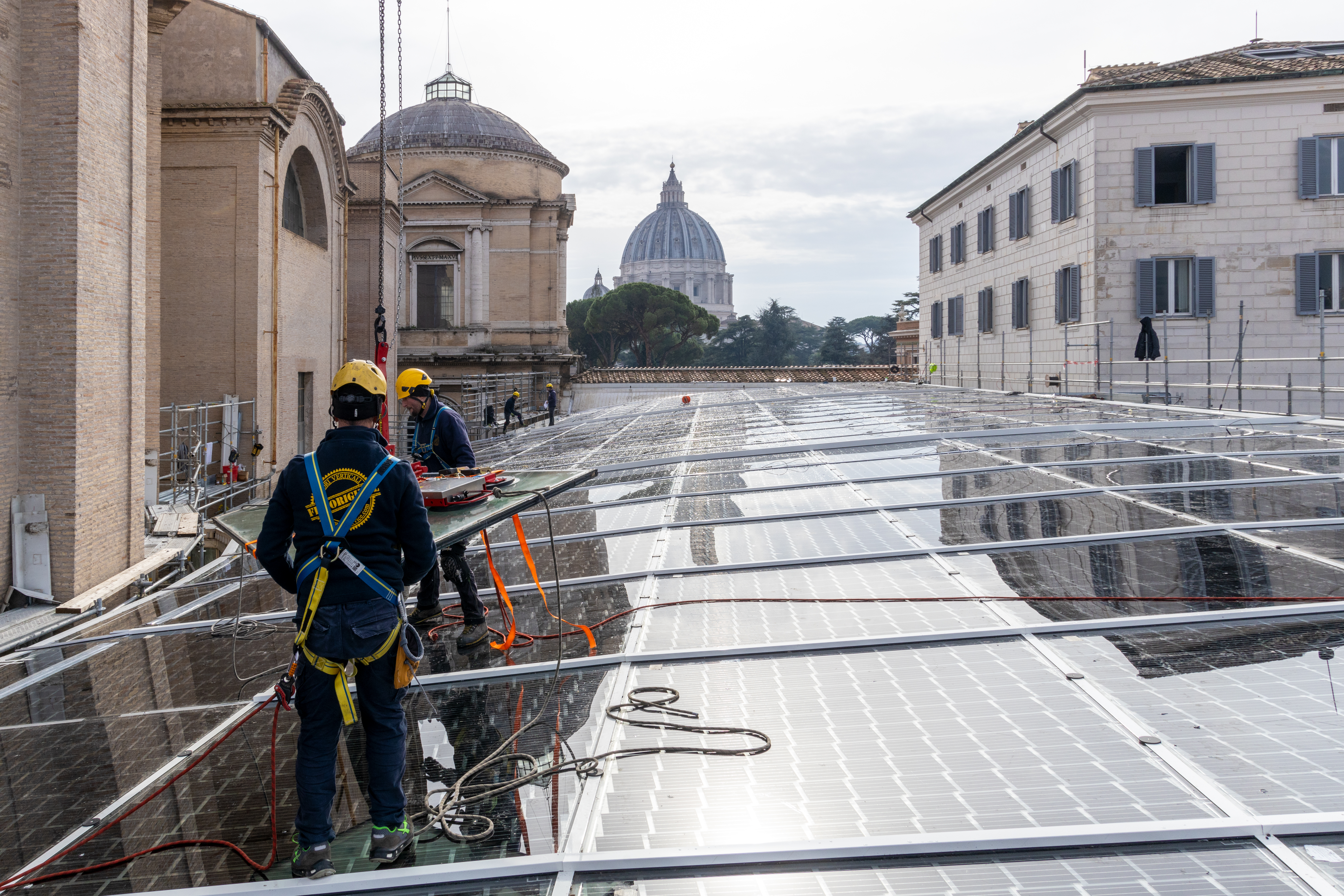 due operai che installano i pannelli fotovoltaici con la basilica di san pietro che si vede in lontananza